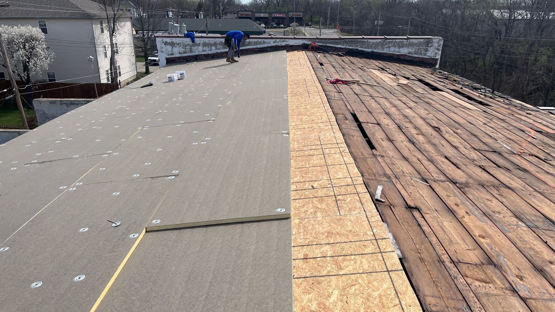 Half-completed roof replacement. One side has new material, the other is exposed wooden boards. A worker is visible.