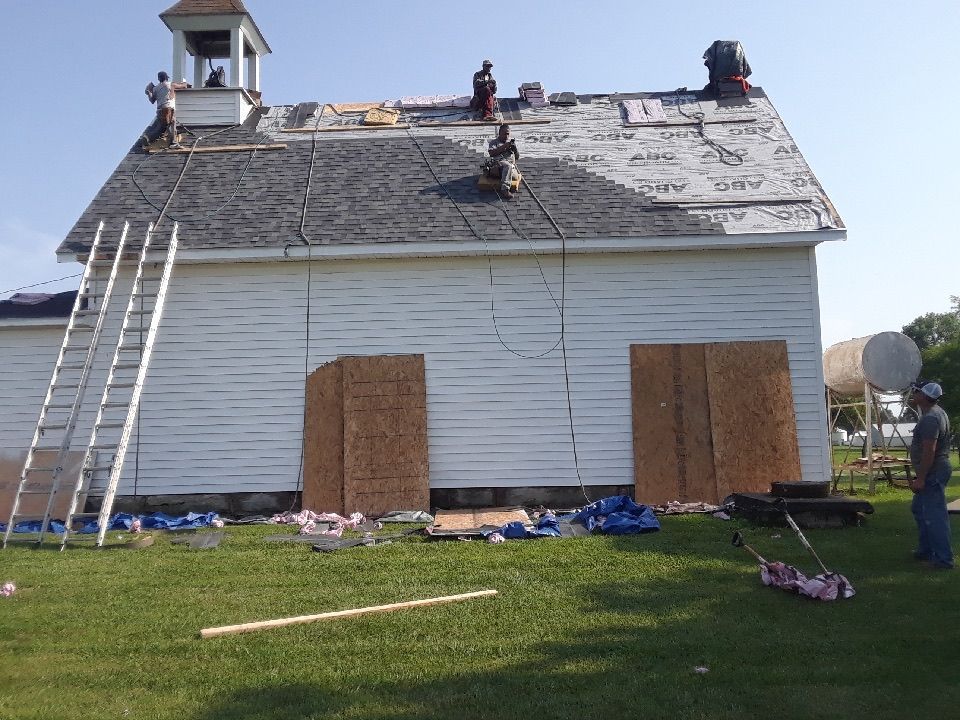 Workers roofing a white building with a small tower; ladder leans against the side.