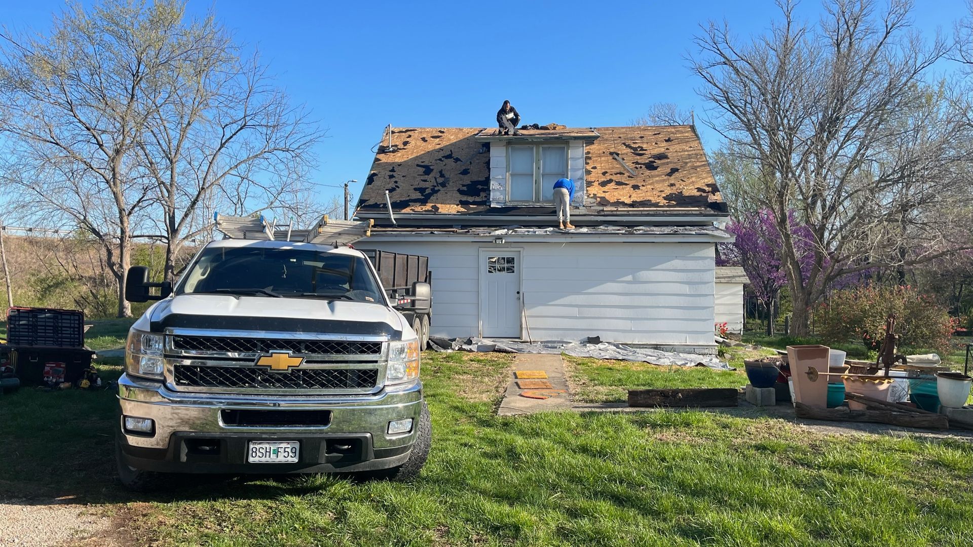 White truck parked in front of a small house with workers on the roof removing shingles.