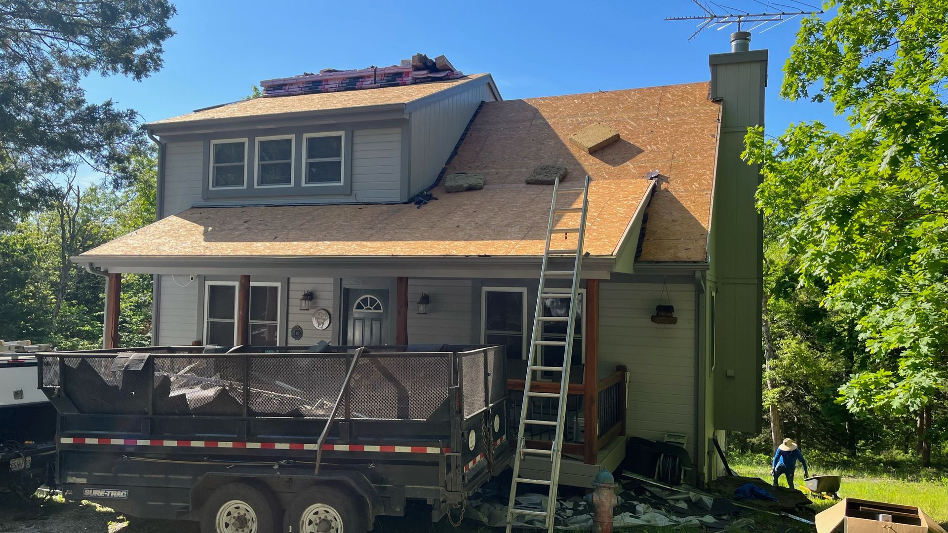 Two-story house with roof replacement in progress, ladder, and trailer.