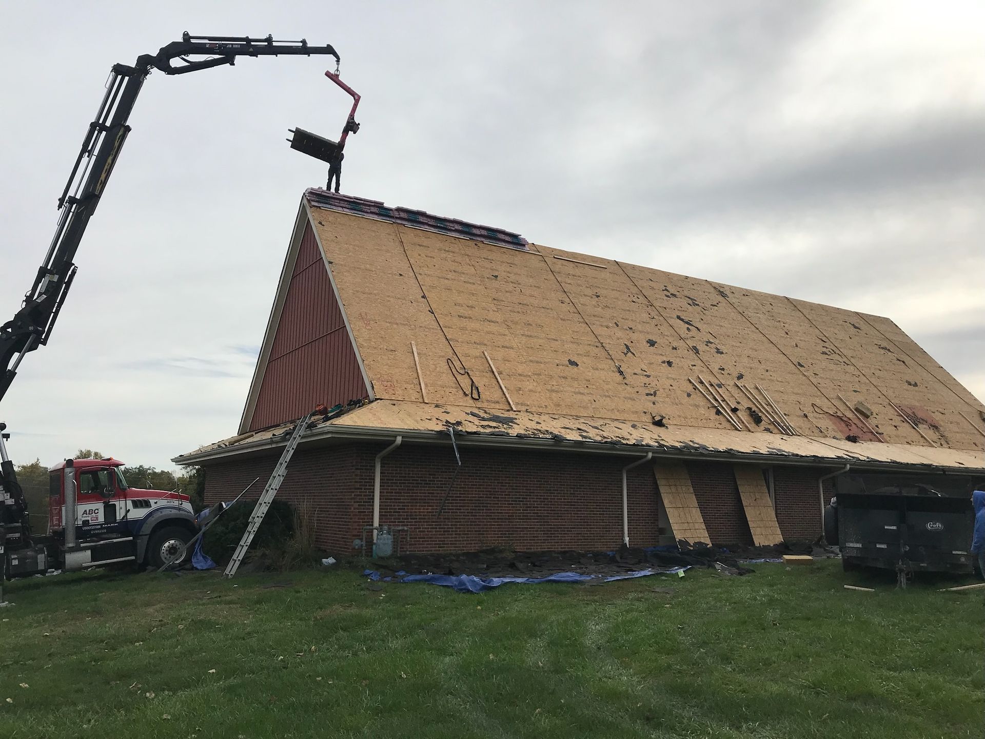 Barn under construction with a crane. The roof is being worked on in a grassy field.