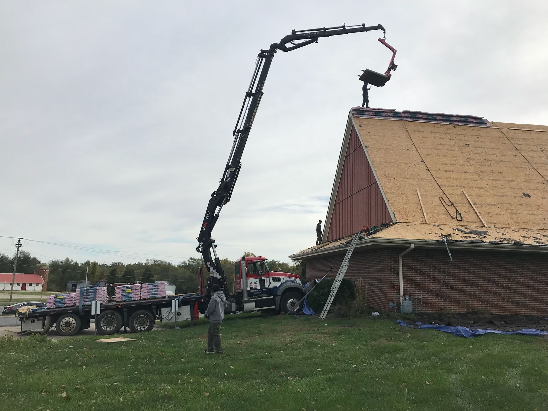 Concrete pump truck pouring concrete onto a roof. Workers in yard. Cloudy sky.