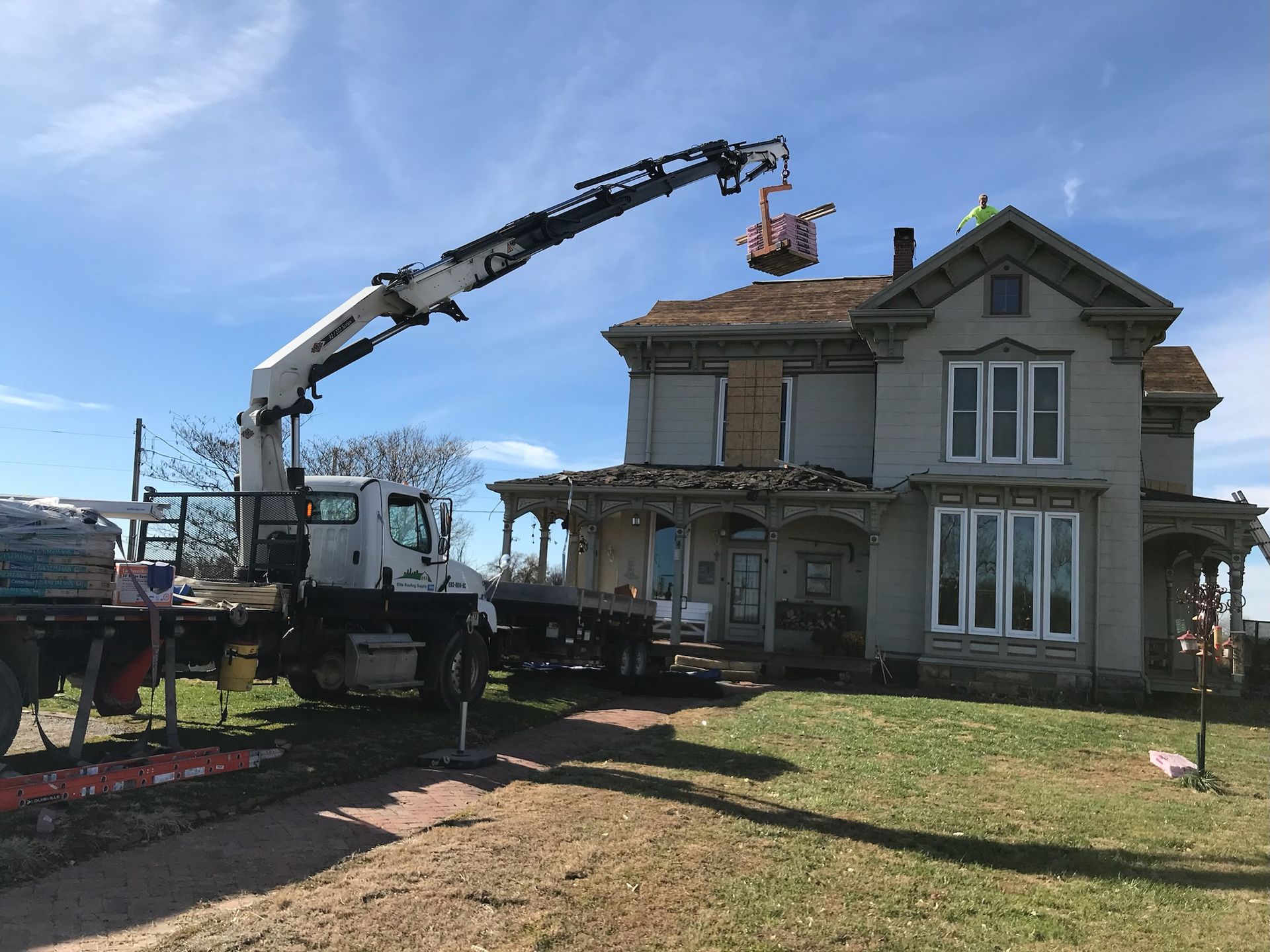 A truck with a crane lifting a person in a bucket basket to work on a two-story house roof, outdoors.