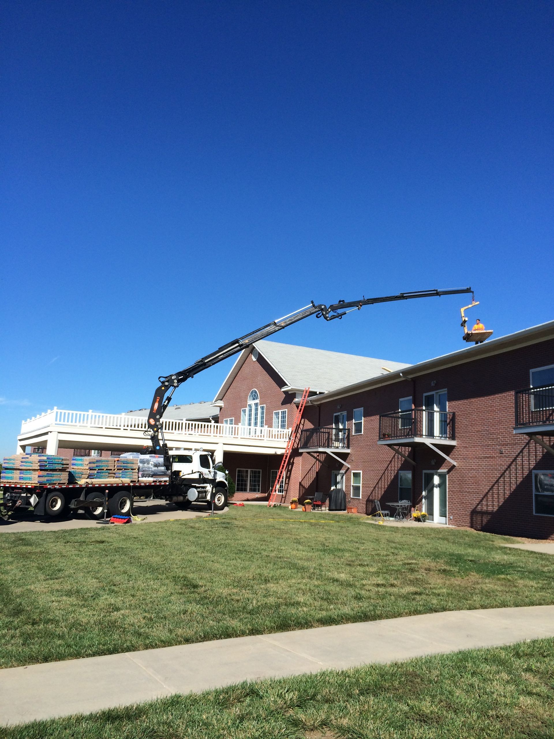 A crane lifting materials onto a brick building with a truck on the lawn. Blue sky.