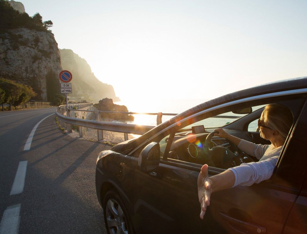 Una donna sta guidando un'auto lungo una strada con il braccio fuori dal finestrino.