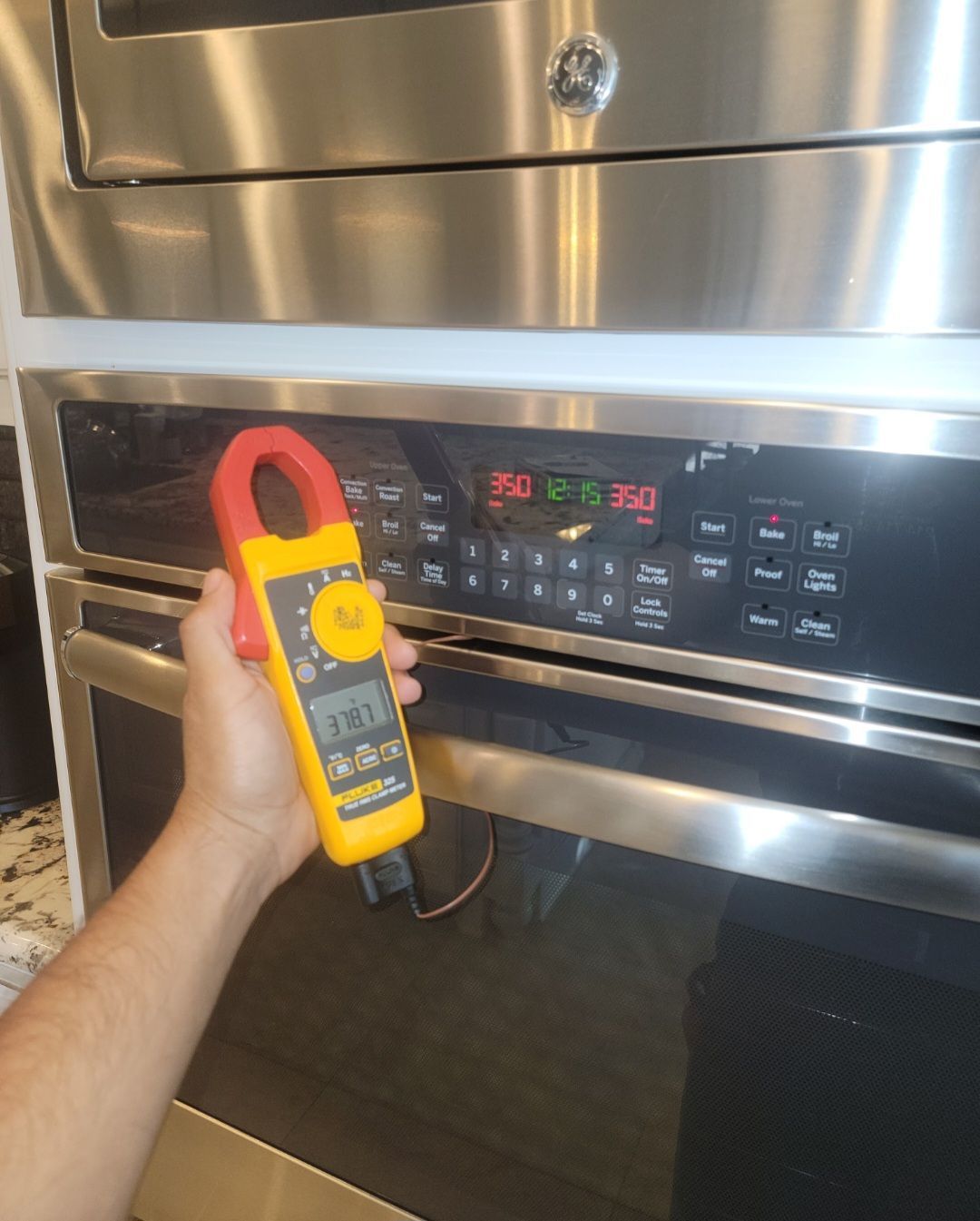 A person is holding a clamp meter in front of an oven.