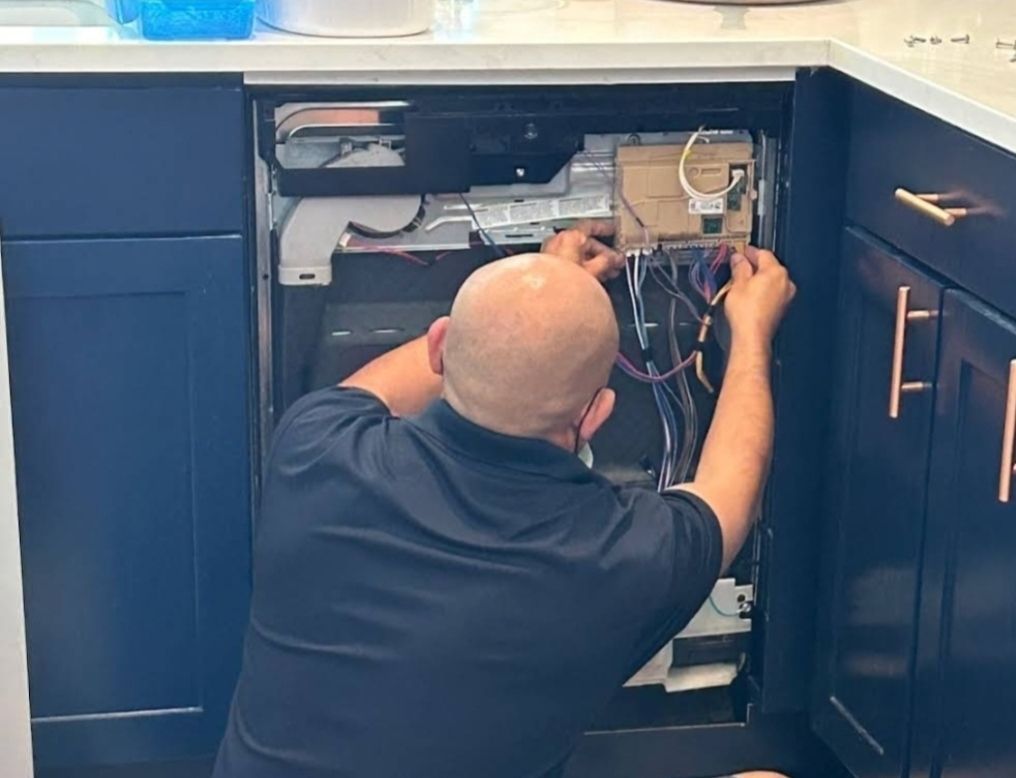 A man is working on a dishwasher in a kitchen.