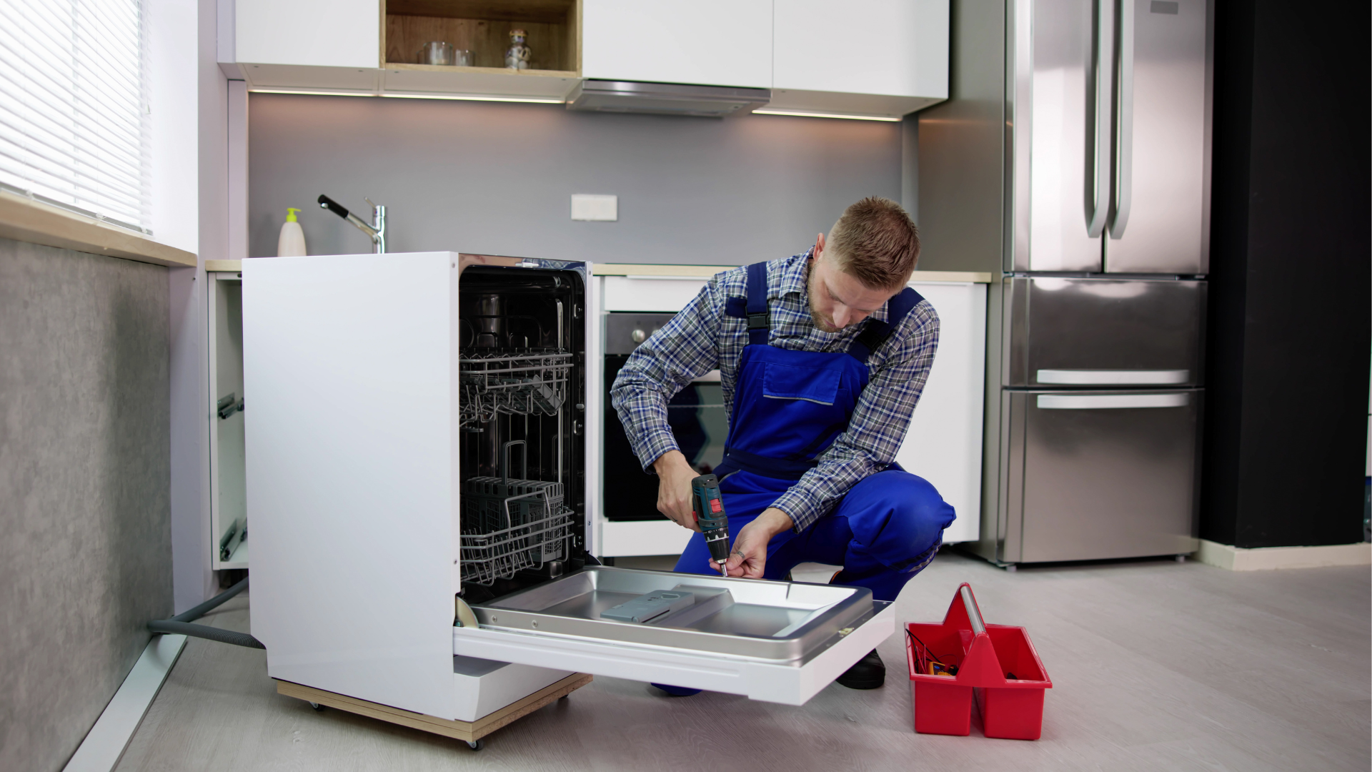 A man is fixing a dishwasher in a kitchen.