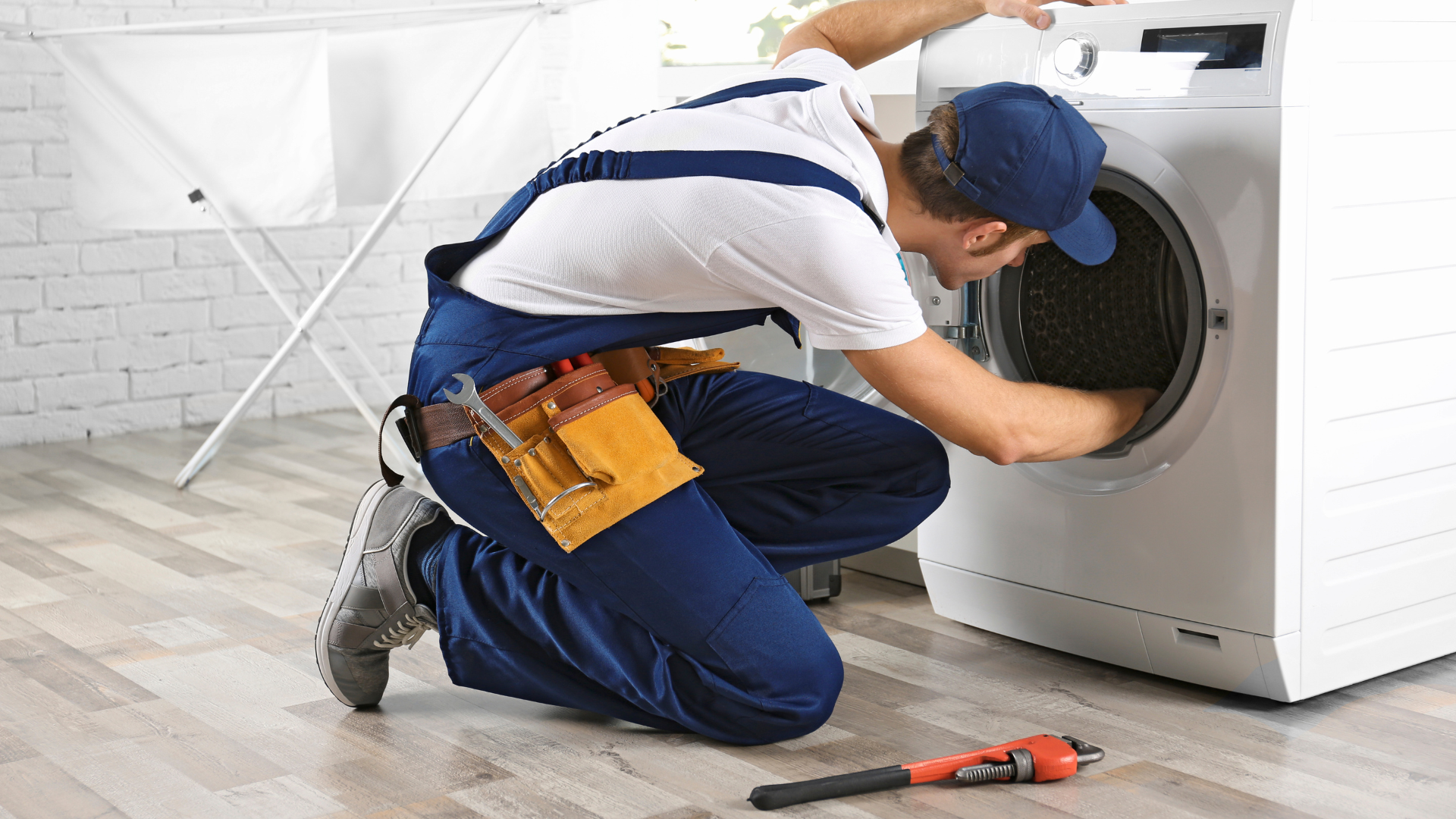 A man is fixing a washing machine in a laundry room.