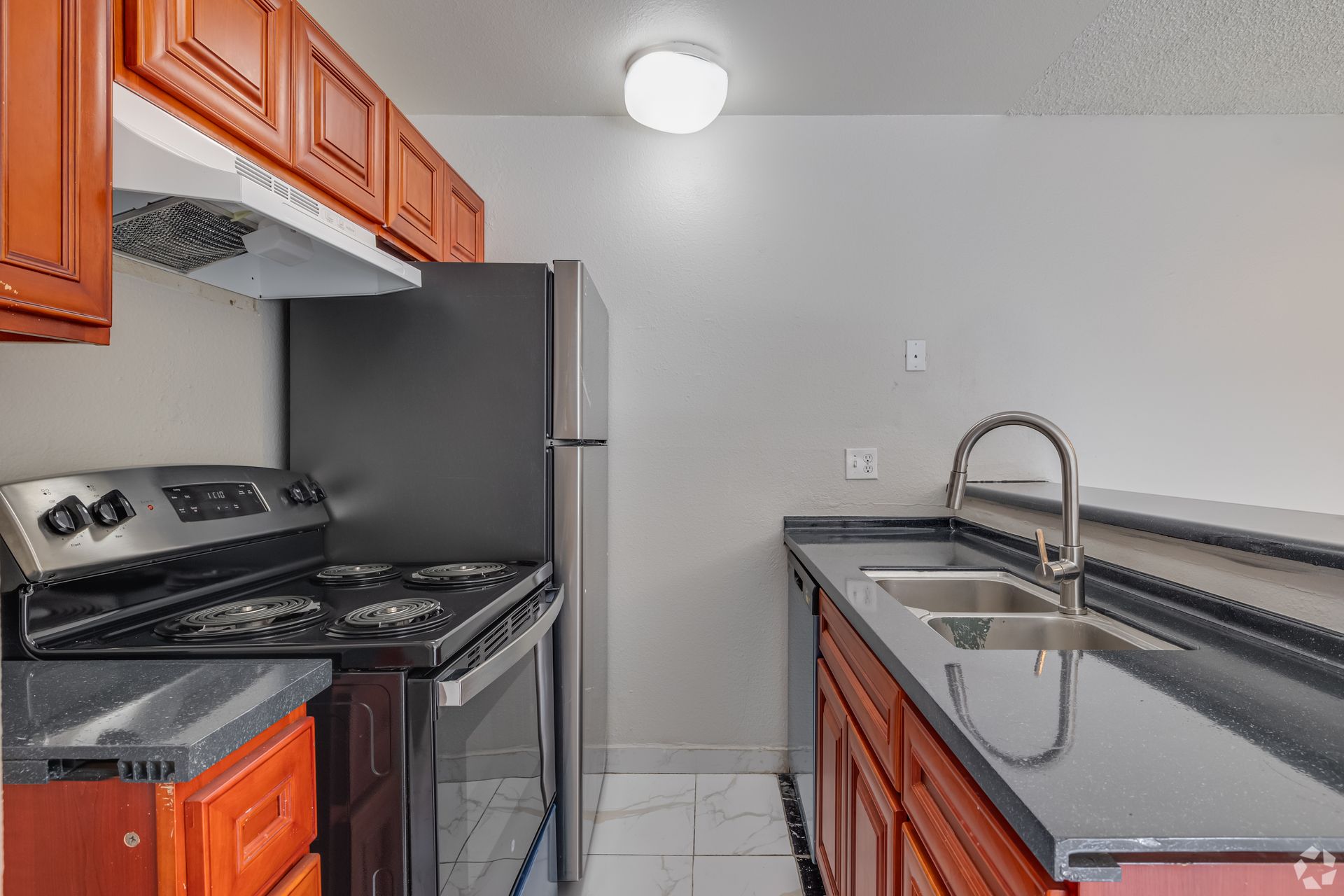 Kitchen with dark countertops, stainless steel appliances, and reddish-brown cabinets.