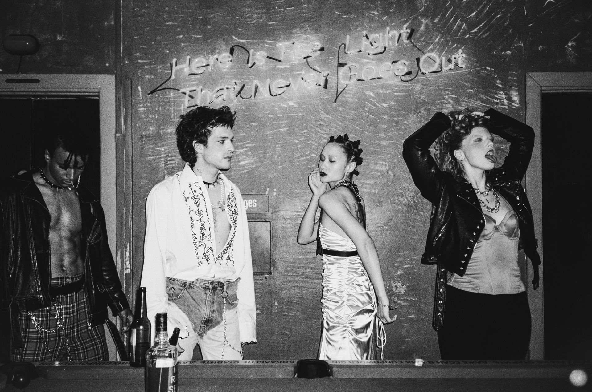 Four people pose by a pool table in a dimly lit room. Graffiti behind them.