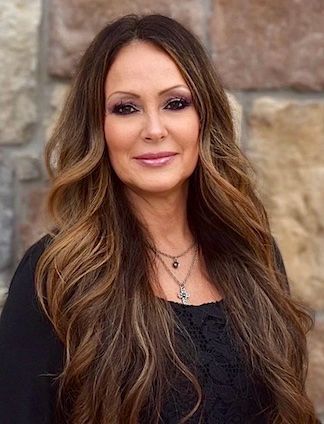 A woman is sitting at a desk with a laptop and a vase of flowers.