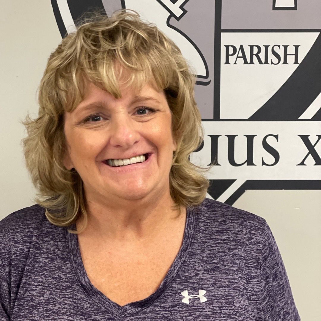 A woman in a purple shirt is smiling in front of a parish logo