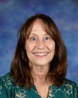 A woman is smiling while standing in front of a tree.