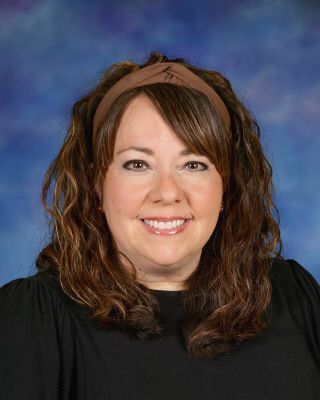 A woman in a pink shirt is standing next to a tree and smiling.