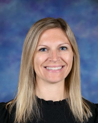 A woman in a pink shirt is standing in front of a tree.