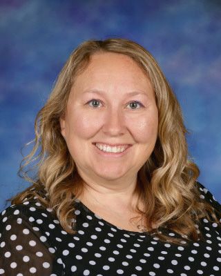 A woman in a zebra print shirt is smiling and standing next to a tree.