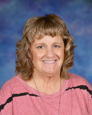 A woman in a striped shirt is smiling while standing next to a tree.
