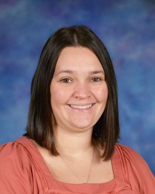 A woman in a blue shirt is standing in front of a tree.