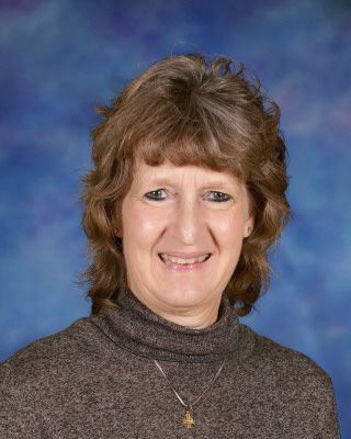 A woman in a white shirt is smiling in front of a tree.