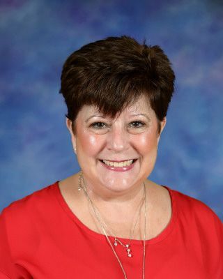 A woman is smiling in front of a brick building.