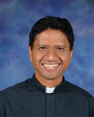 A man in a black shirt with a white collar is smiling for the camera.