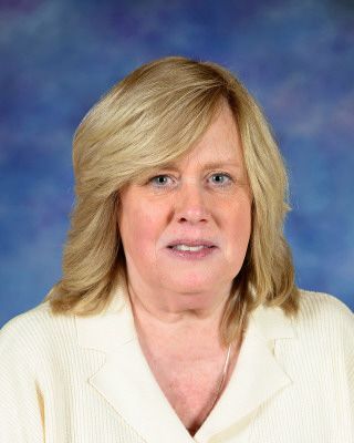 A woman in a striped shirt is smiling in front of a tree.