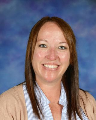 A woman wearing overalls and a white shirt is smiling for the camera.