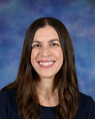 A woman in a denim jacket is smiling in front of a sign that says st. p. sc