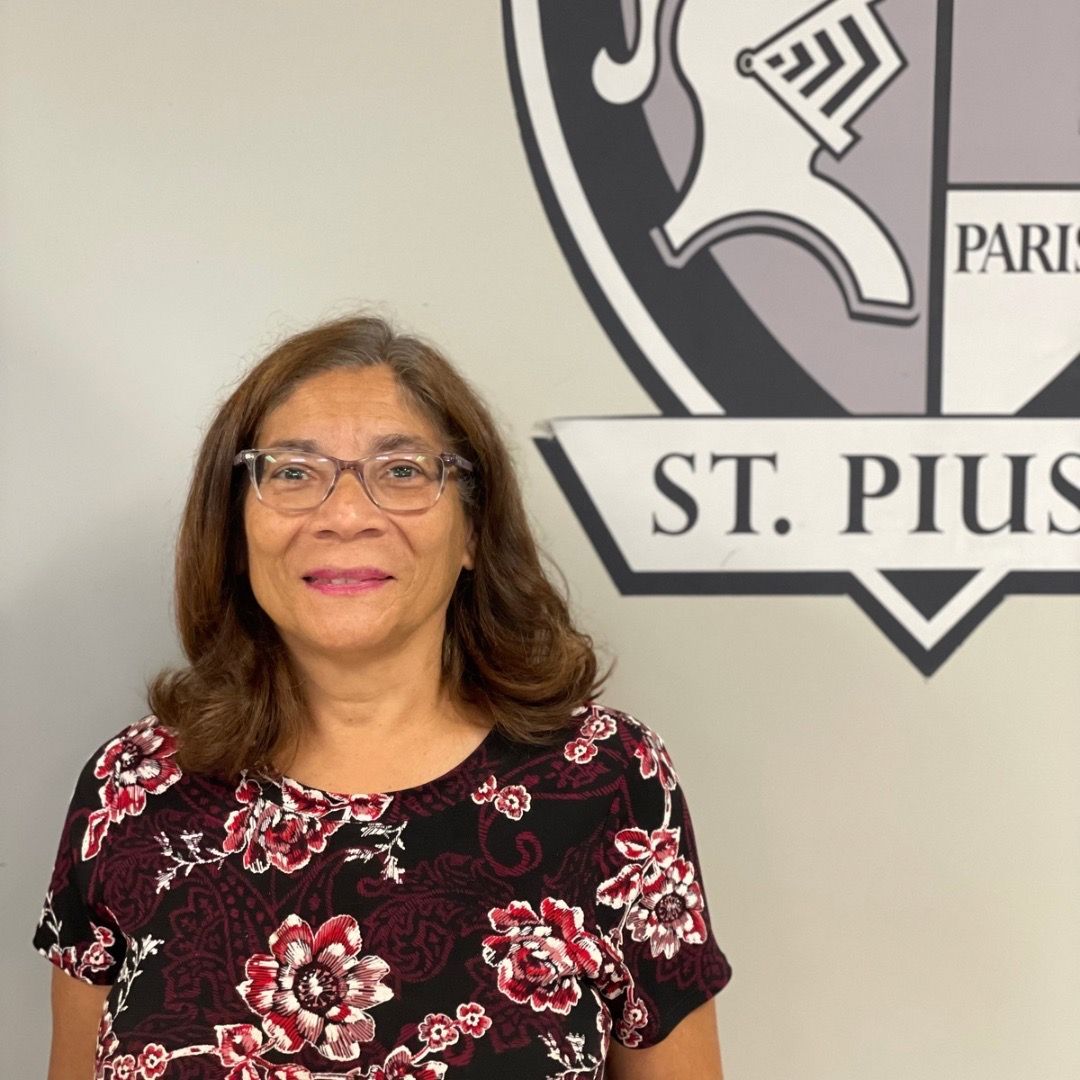 A woman wearing glasses is standing in front of a sign that says st. pius