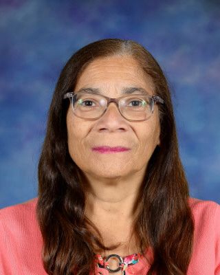 A woman wearing glasses is standing in front of a tree.