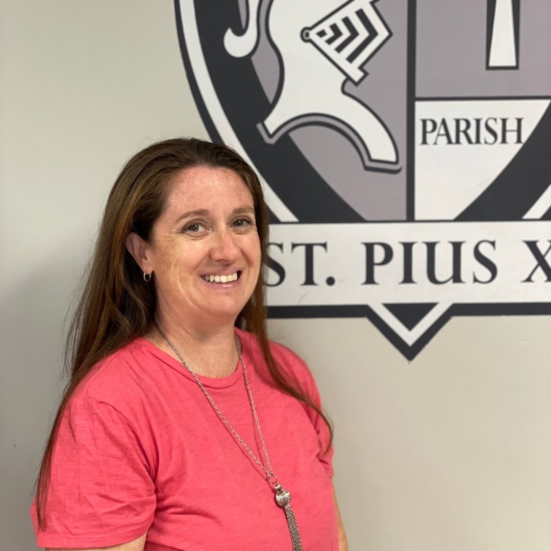 A woman in a pink shirt is smiling in front of a parish logo