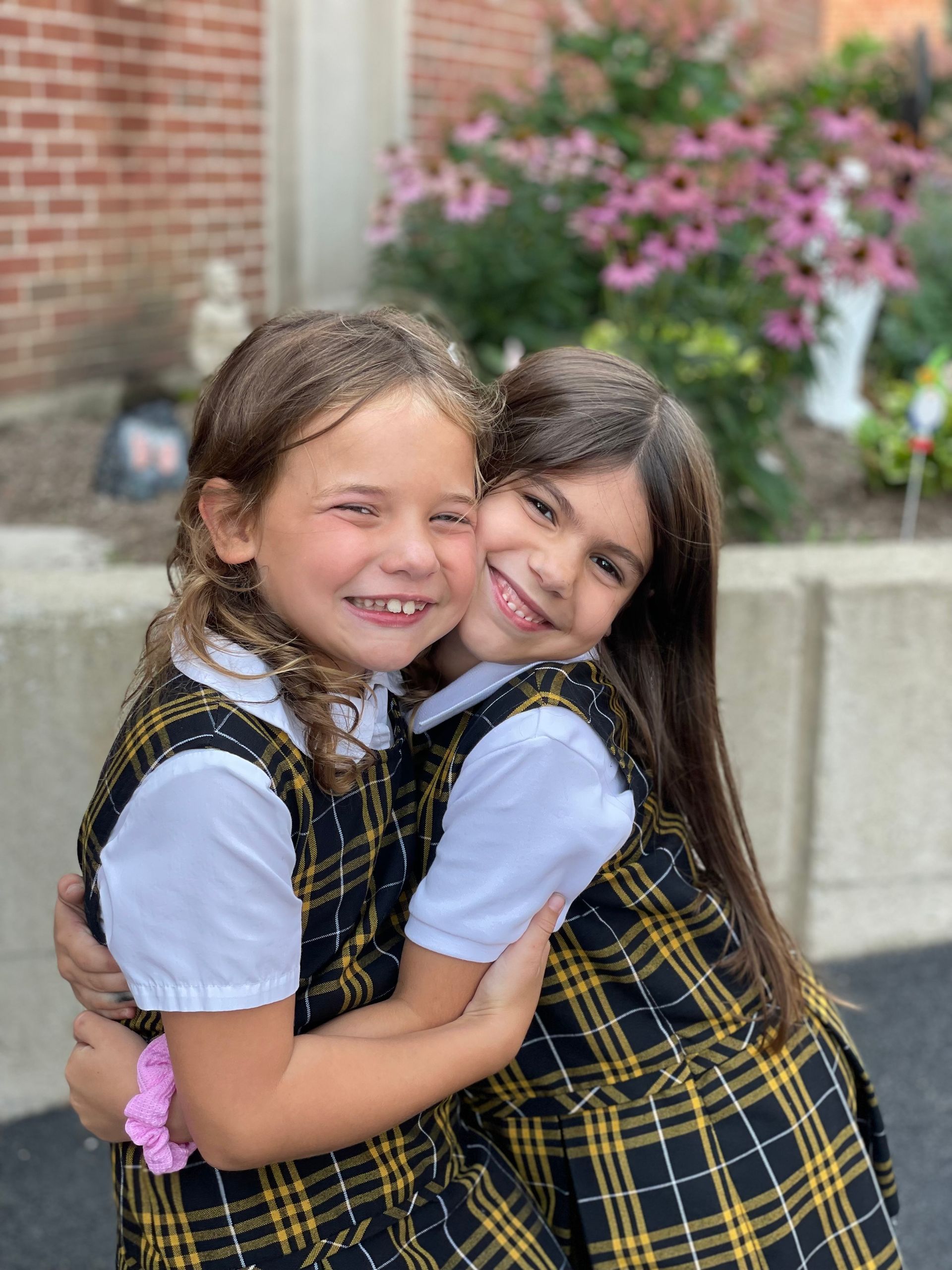 Two little girls are hugging each other in front of a brick building.