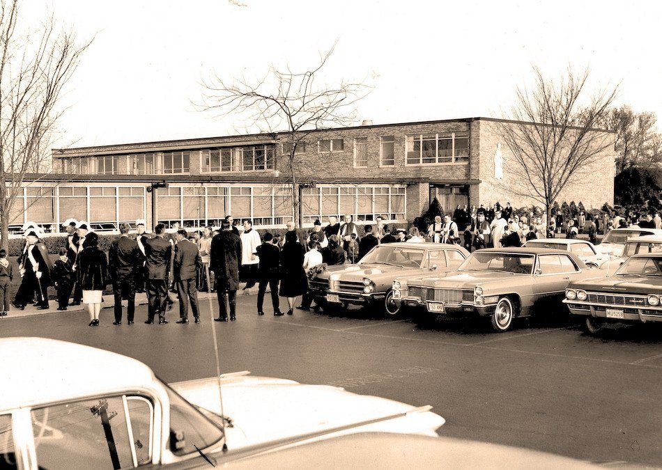 A black and white photo of a parking lot with cars parked in front of a building