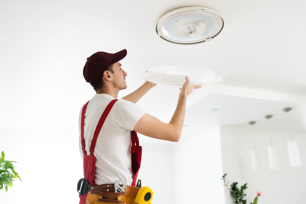 A man is installing a ceiling light in a living room.