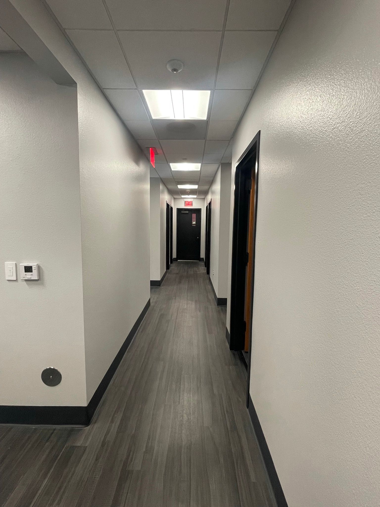 A long hallway in a building with a red exit sign on the ceiling.