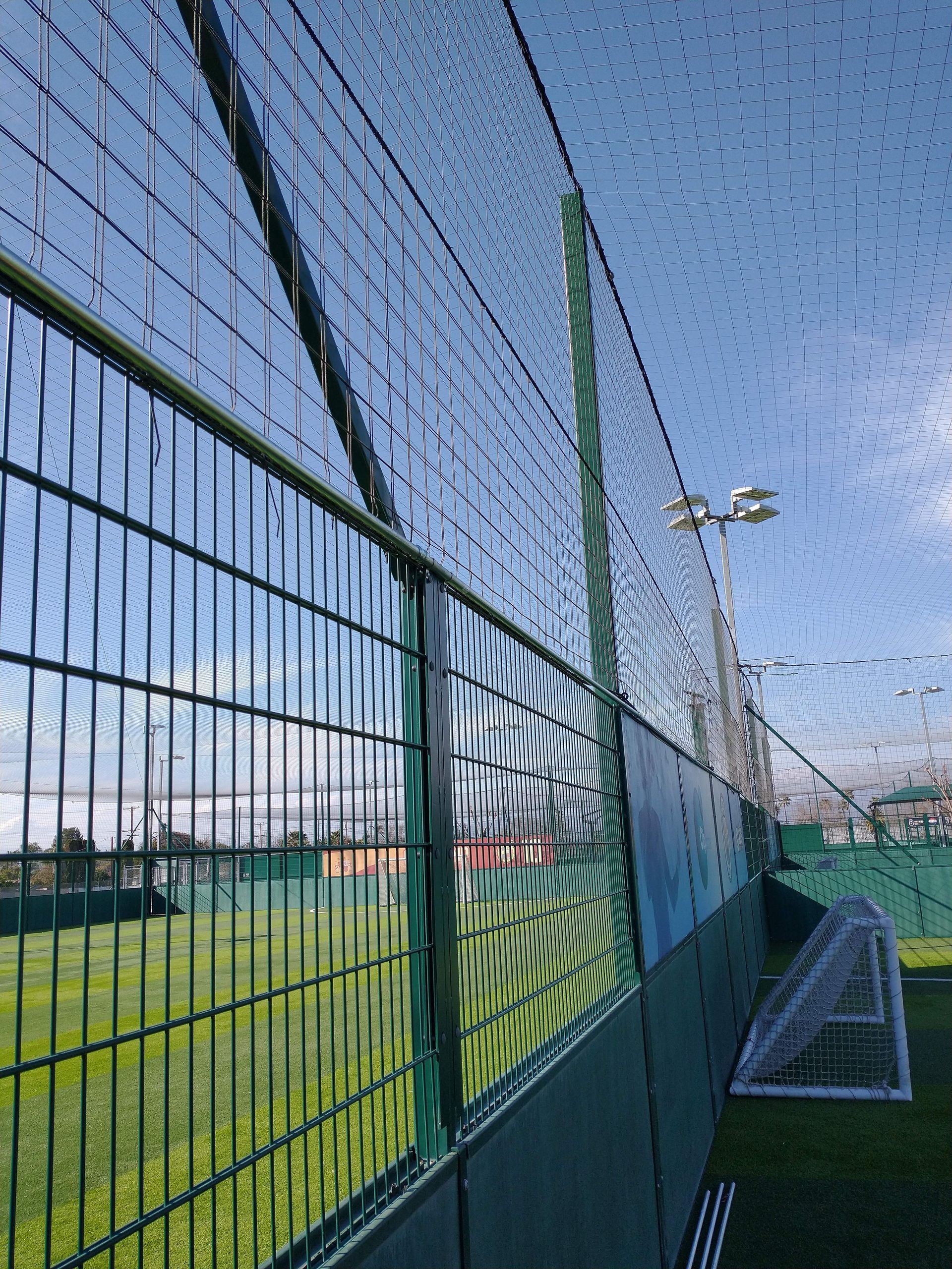 A fence surrounds a soccer field with a blue sky in the background