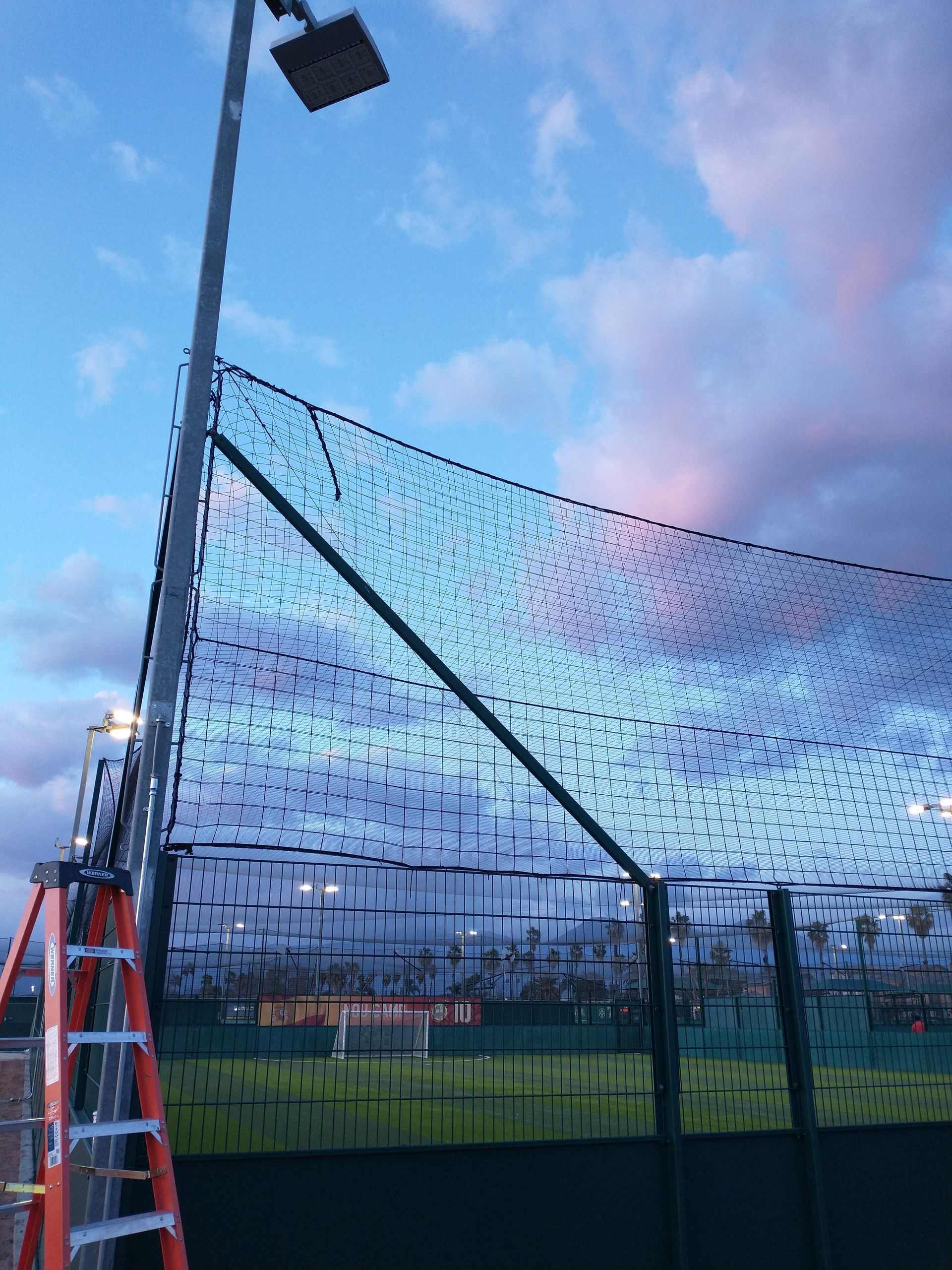 A ladder is sitting next to a baseball net