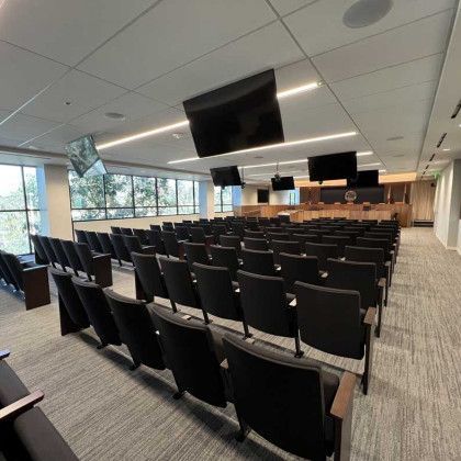 A large auditorium with rows of black chairs and televisions on the ceiling.