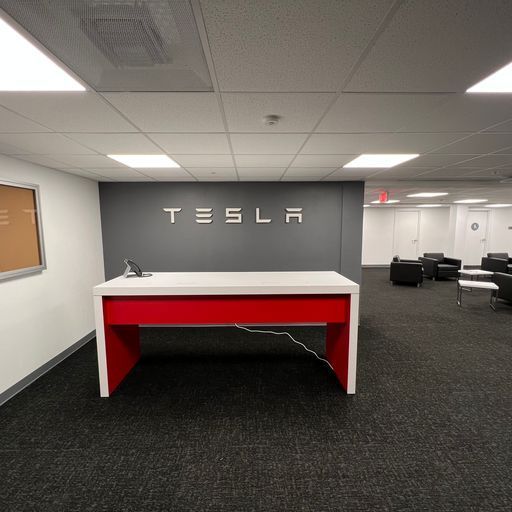 A tesla office with a red desk and a tesla logo on the wall.