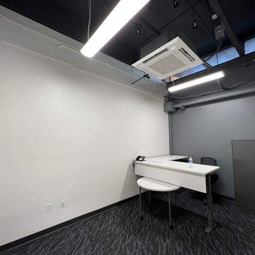 A room with a desk and chairs and a ceiling fan.