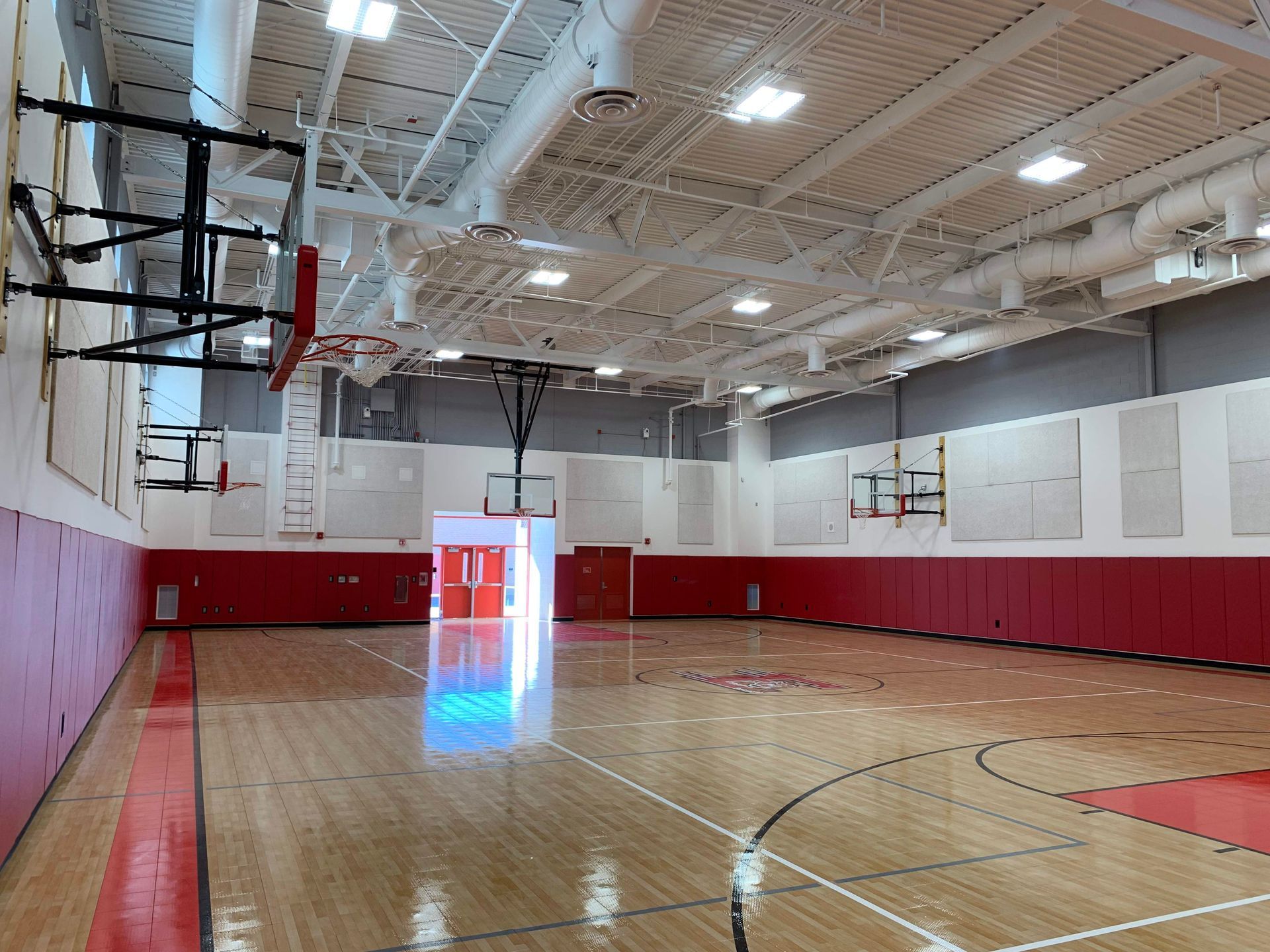 An empty basketball court in a gym with a basketball hoop hanging from the ceiling.