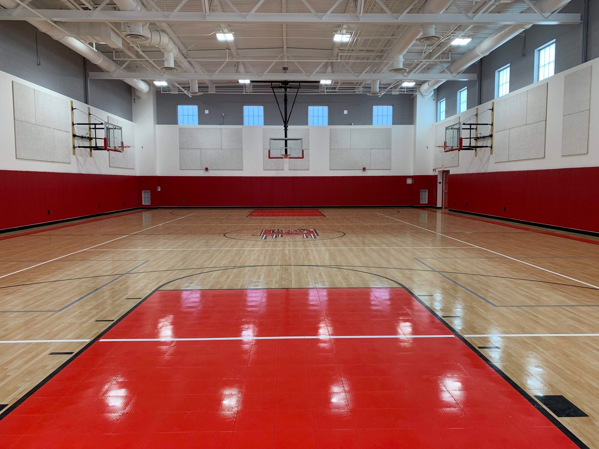 An empty basketball court with a red floor and a basketball hoop.