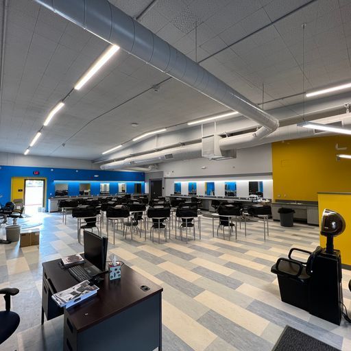 A large room with tables and chairs and a computer on a desk