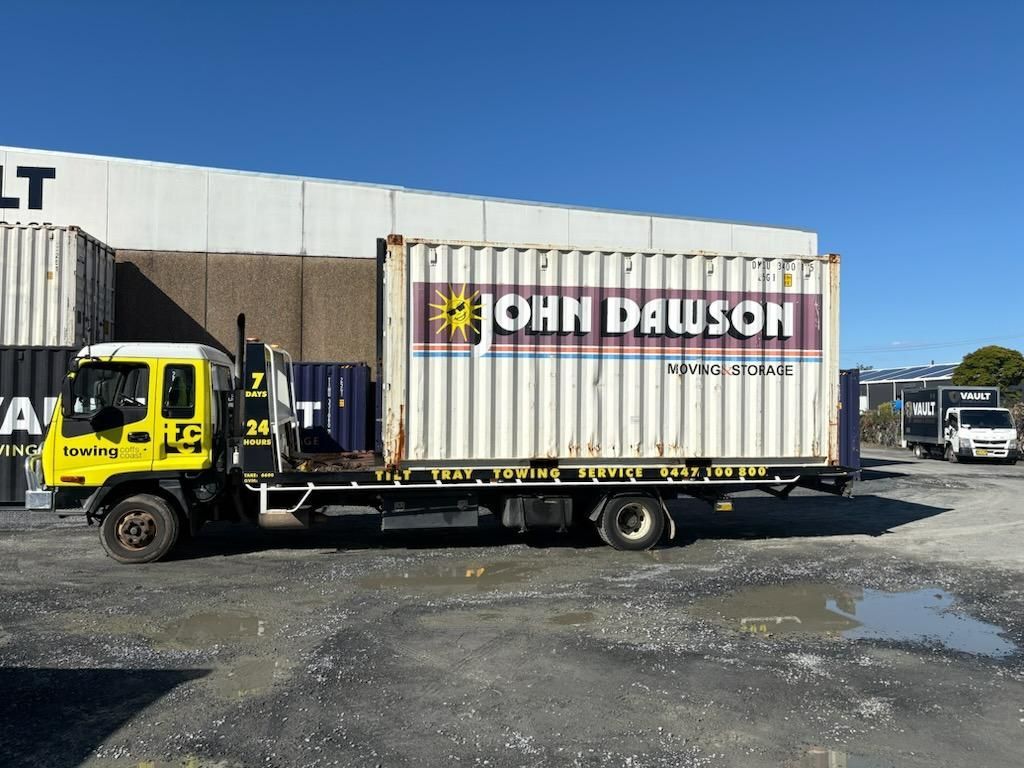 Yellow Truck With a John Dawson Shipping Container on Its Flatbed in a Yard on a Sunny Day — TCC Towing Coffs Coast in Harbour, NSW