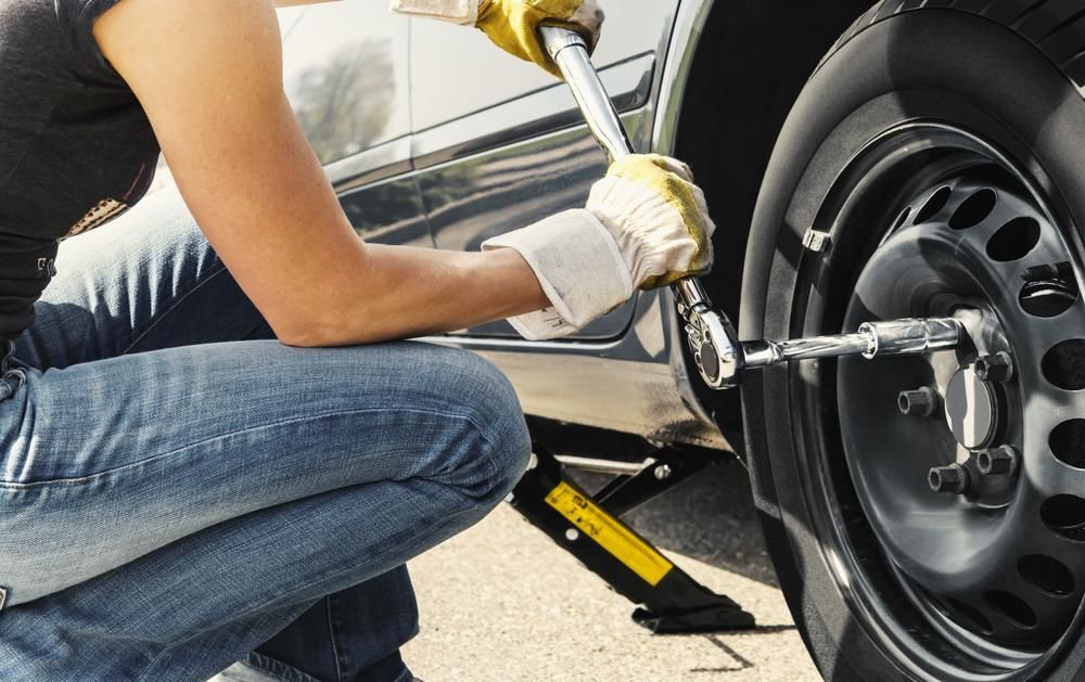 A Woman Is Changing a Tire on A Car with A Wrench — TCC Towing Coffs Coast in Harbour, NSW