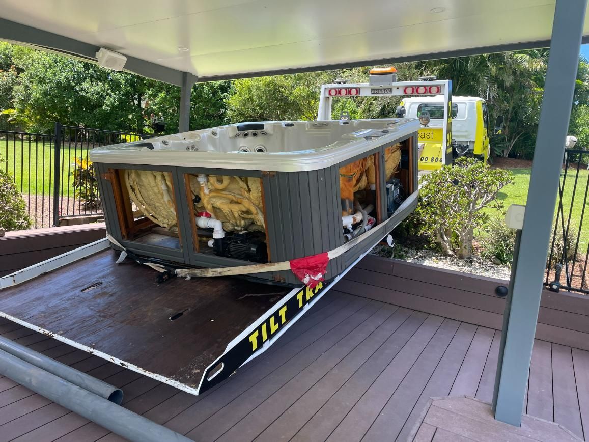 A Hot Tub Being Transported on a Tilt Tray Tow Truck in a Backyard, Covered by a Carport — TCC Towing Coffs Coast in Harbour, NSW