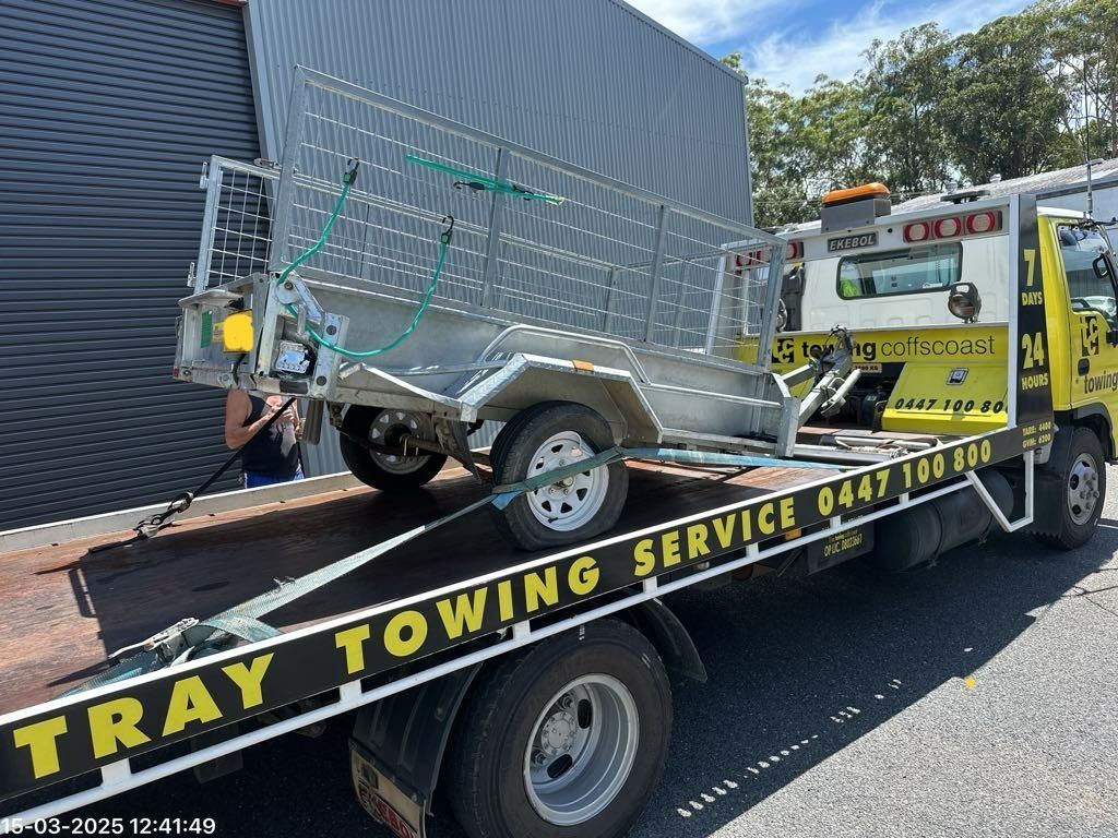 A Yellow Til Towing truck park in carrying a trailer
