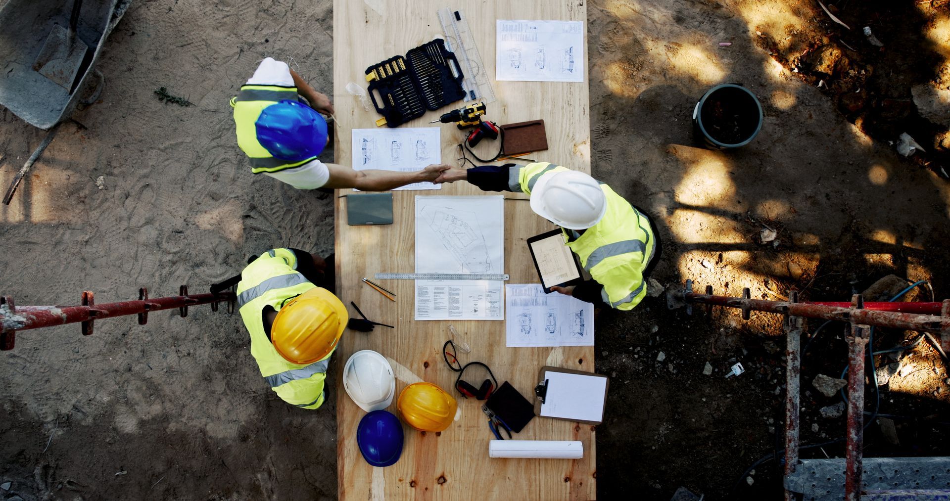 Des ouvriers du bâtiment se rassemblent autour d'une table en bois avec des plans, des outils et des casques.