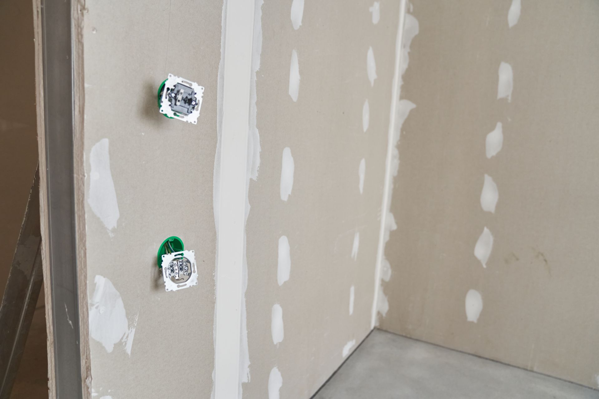 Intérieur en plaques de plâtre avec deux boîtiers électriques. Joints et trous de vis boueux, construction inachevée.